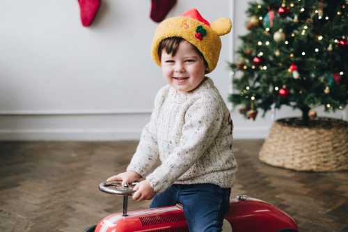 Boy riding a red car next to Christmas tree