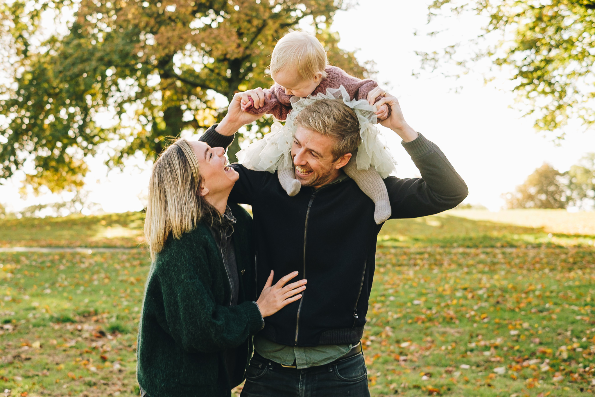 Family all looking at each other, smiling in golden Autumnal light at Graves Park