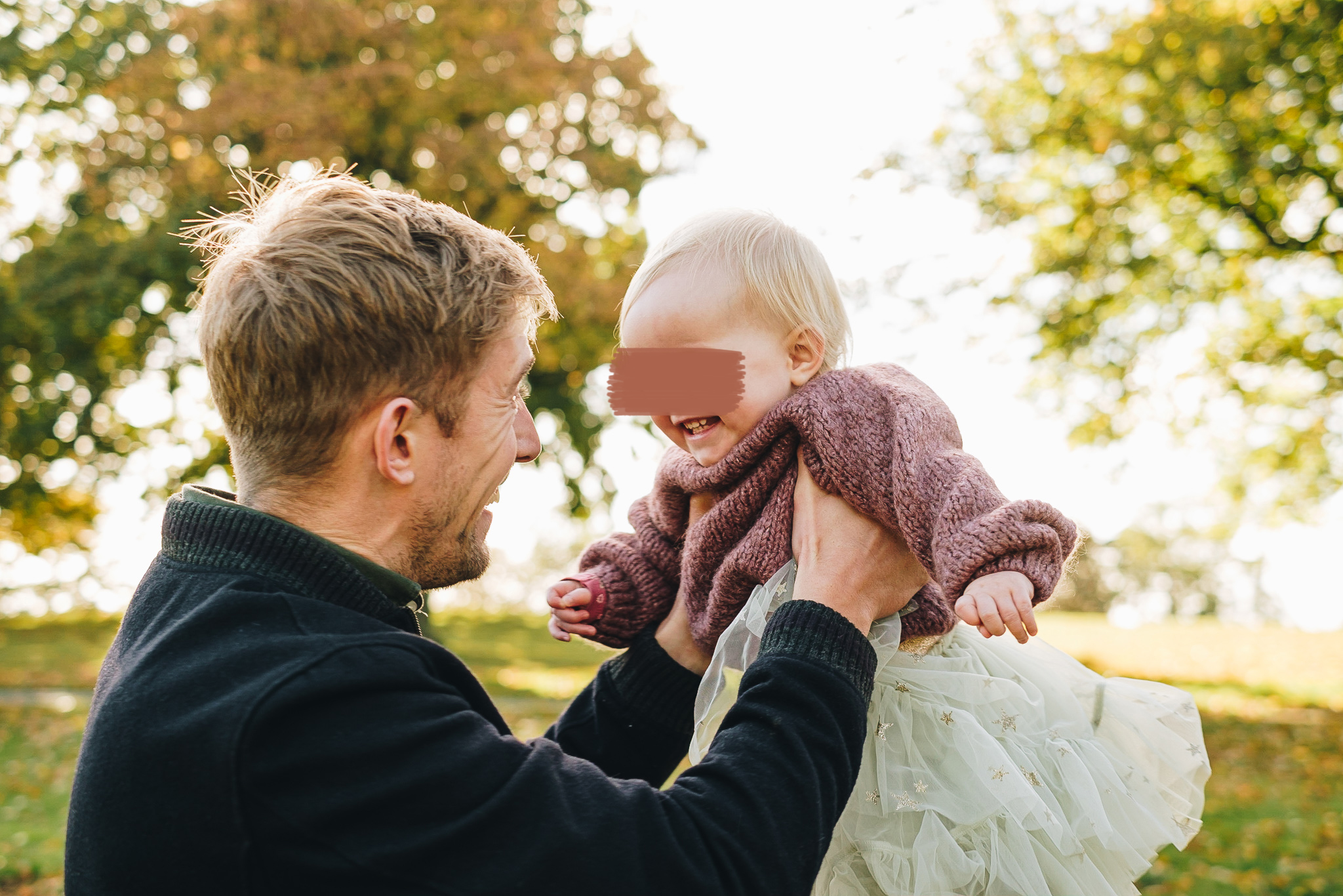 Dad holding daughter while she laughs, surrounded by golden Autumnal light