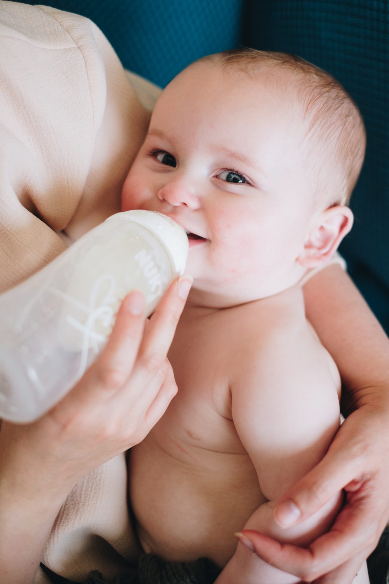 Baby looking directly at camera and smiling while trying to be fed a bottle